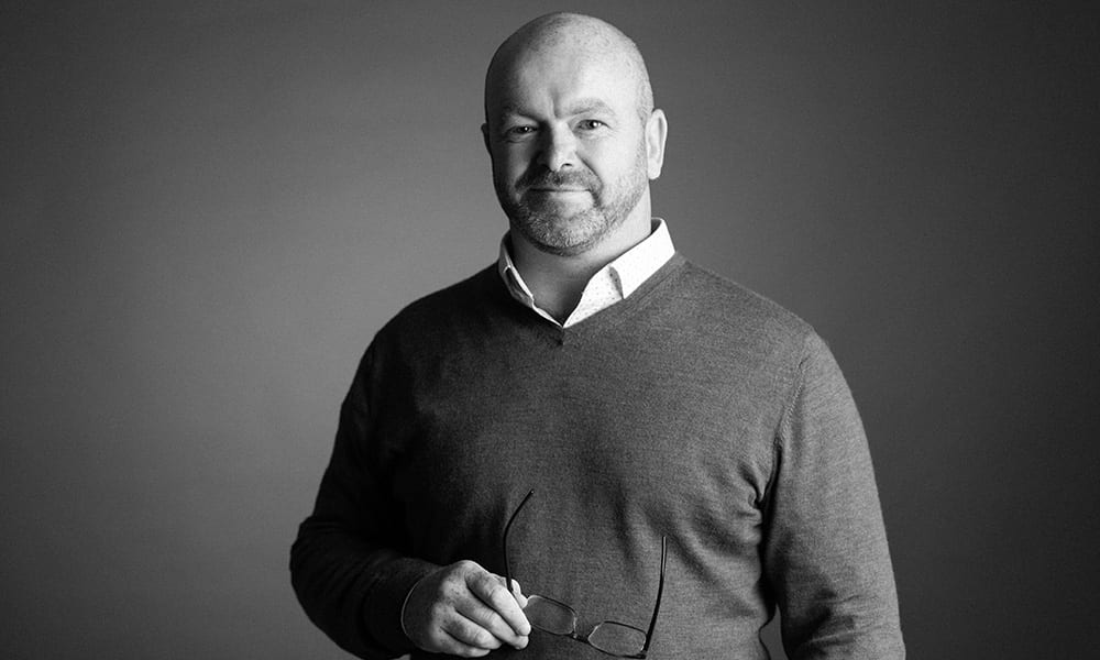 Black and white portrait of a man wearing a sweater against a plain background